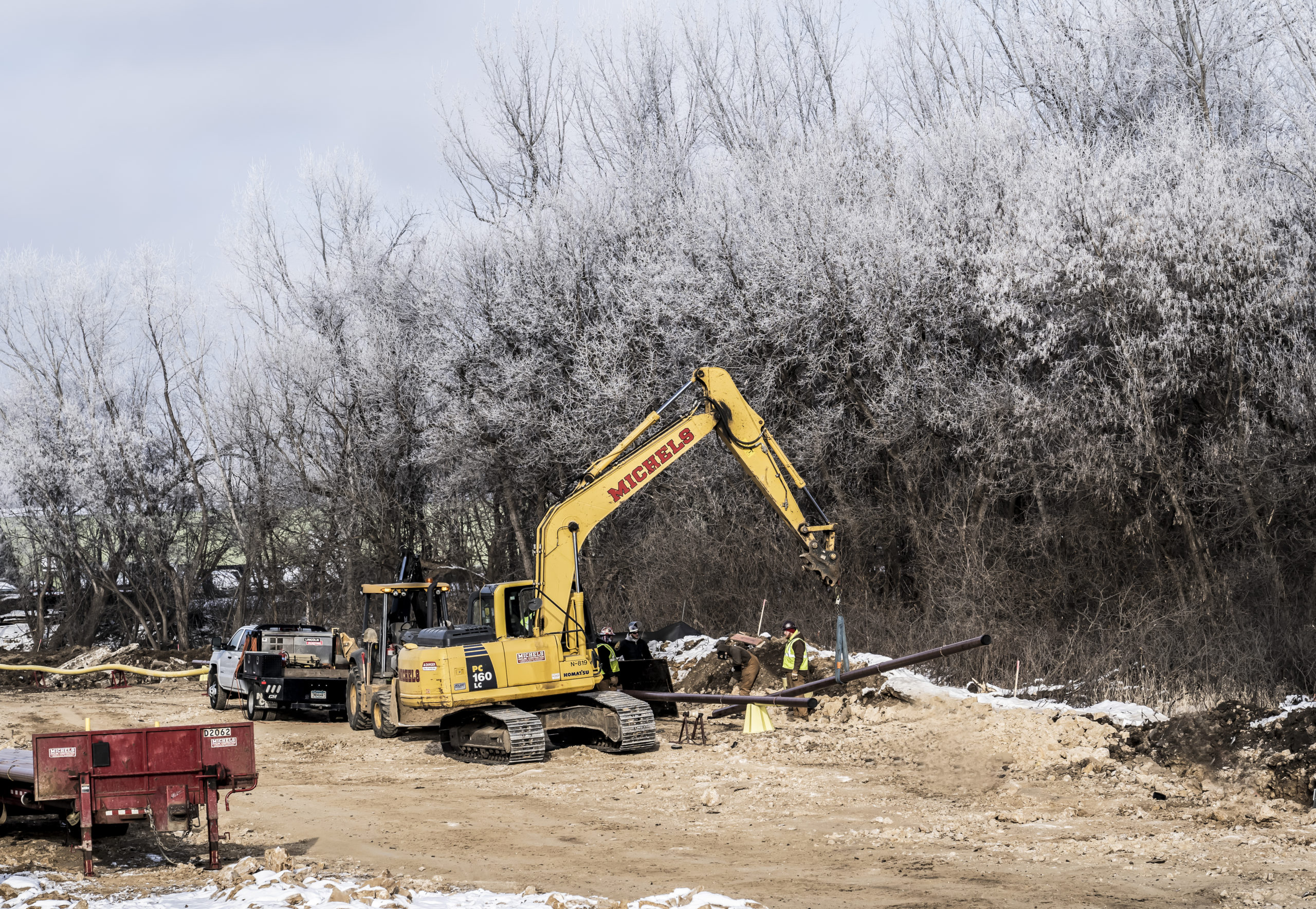 Excavator carries pipe into place on a winter day